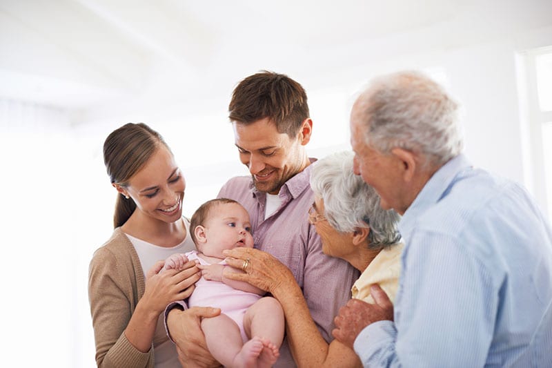 Photo of grandparents and parents smiling at a baby
